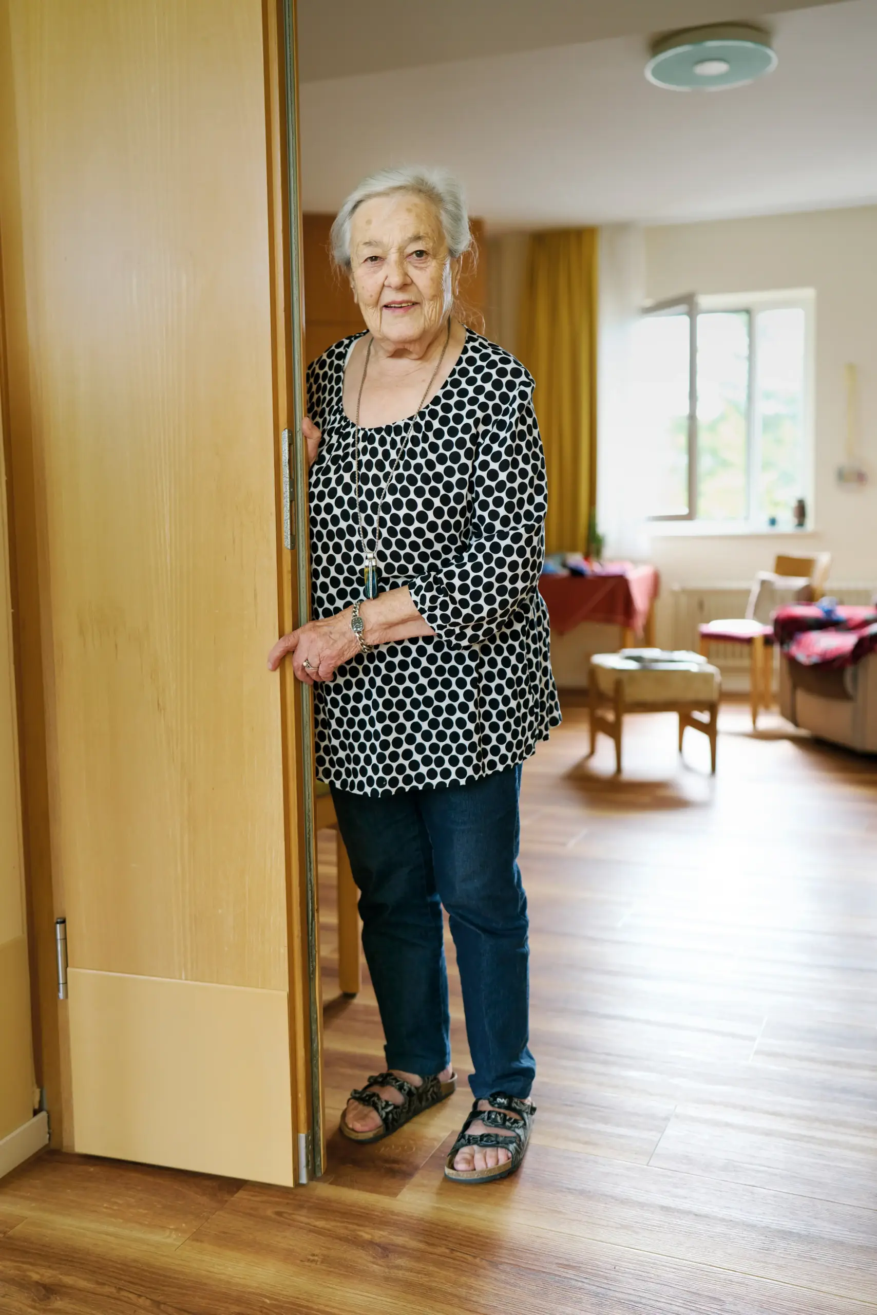 Quelle: BLV Eine ältere Frau steht in einer Türöffnung. Hier ihr kann man ein offenes Fenster und einige Möbel im Zimmer sehen.