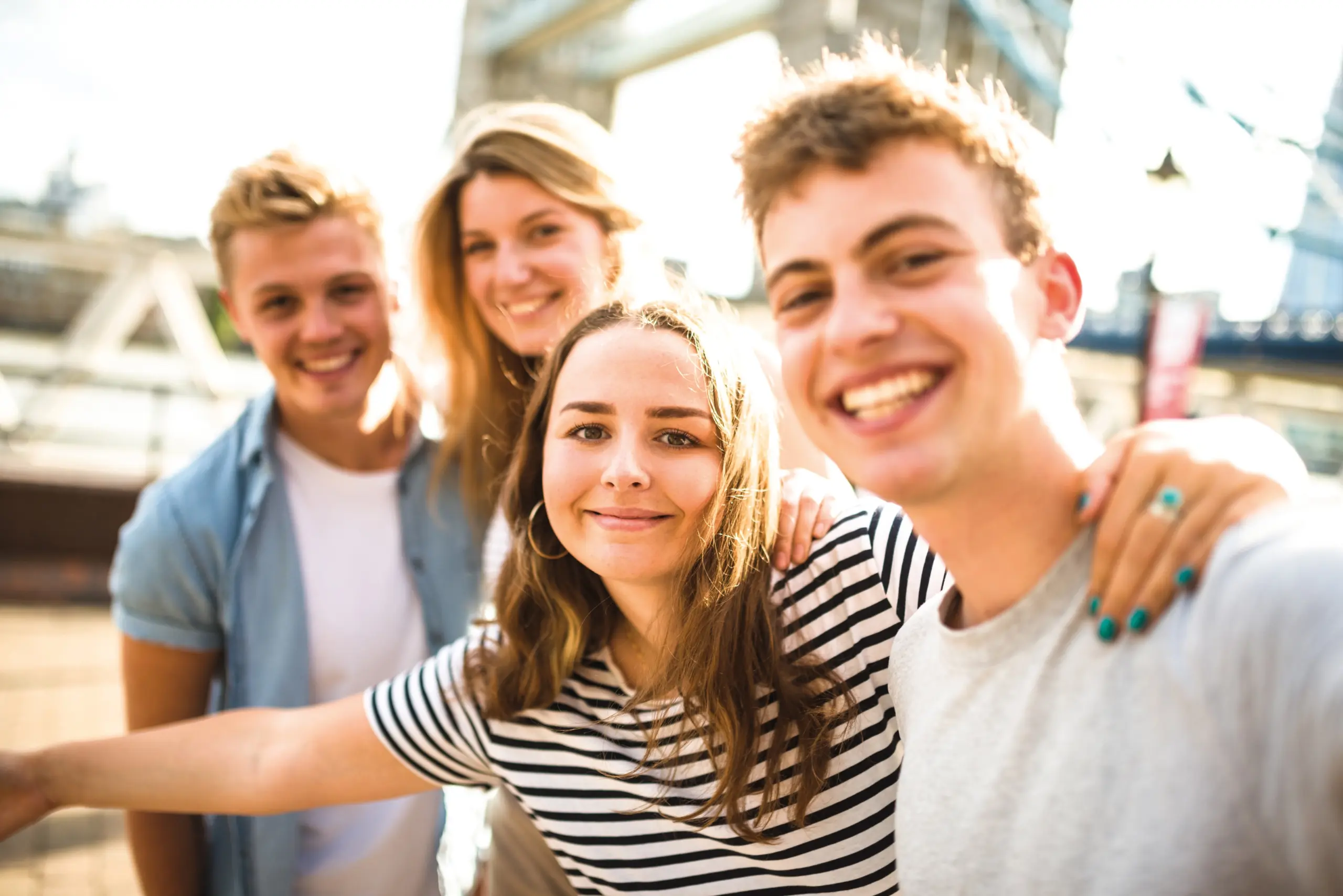Quelle: iStock Vier junge Personen stehen nebeneinander und legen die Arme auf ihre Schultern. Sie lachen.
