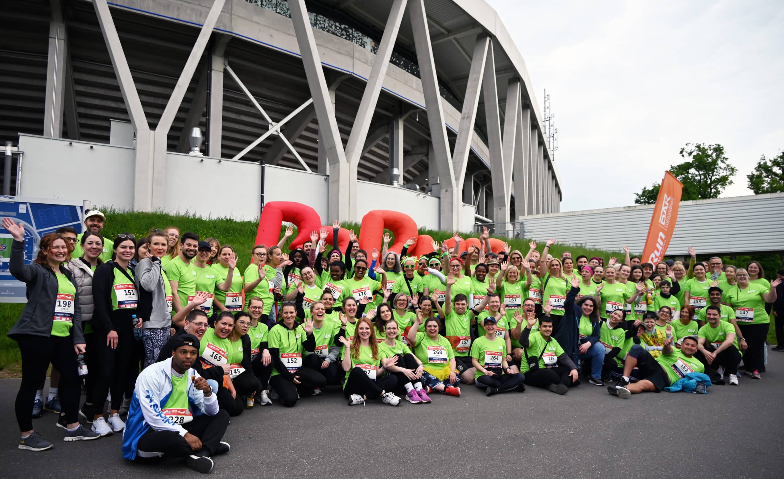 Eine große Gruppe Menschen vor dem Karlsruher Wildparkstadion. Alle tragen ein hellgrünes Shirt mit BLV-Logo. Die Personen haben alle eine Startnummer an ihrer Kleidung befestigt. Sie lachen und winken.