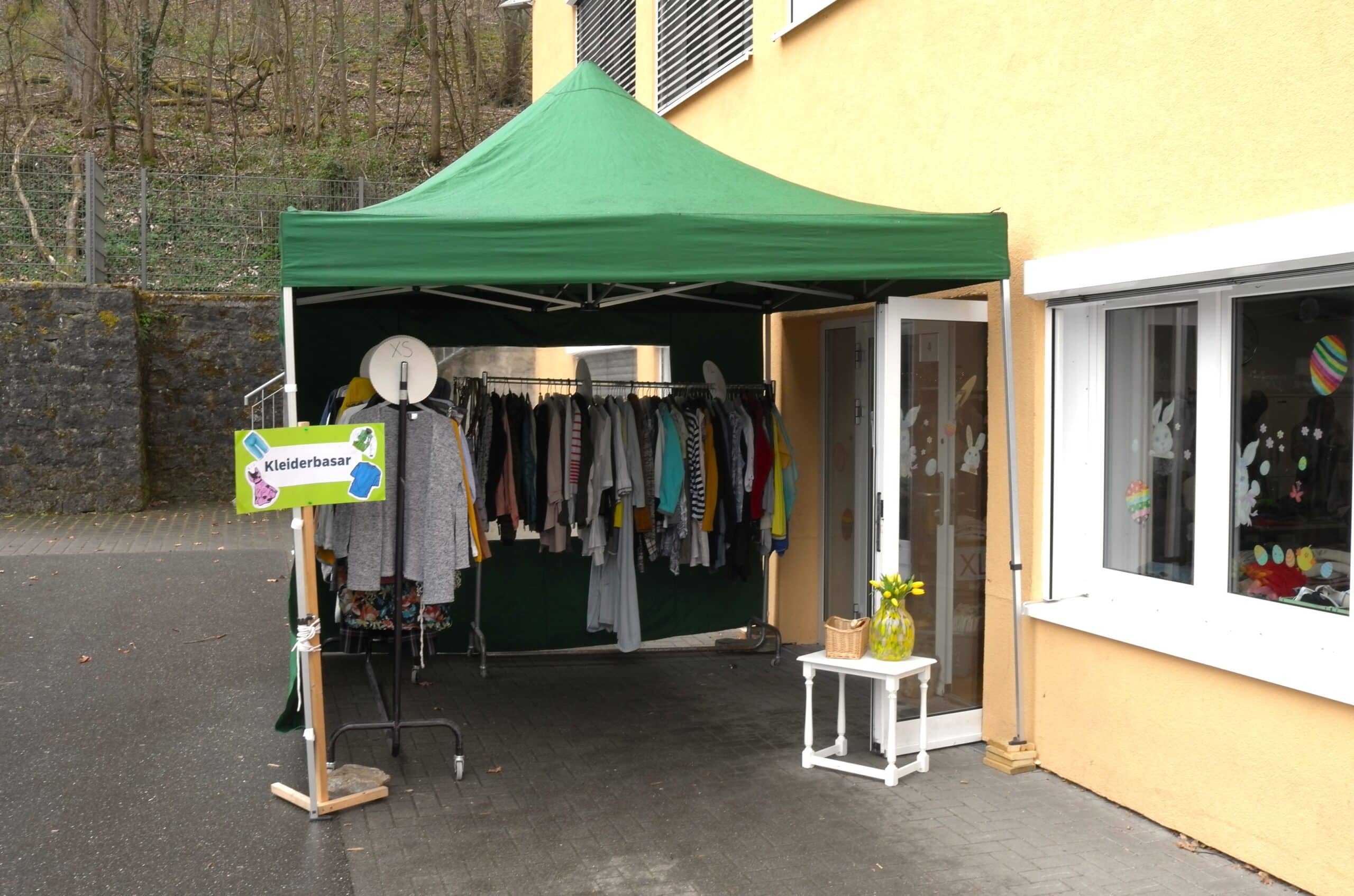Ein grüner Pavillon steht vor dem gelben Gebäude der Schule Enzberg an einer offenen Tür. An einem Pfosten des Pavillons ist ein Schild mit der Aufschrift 