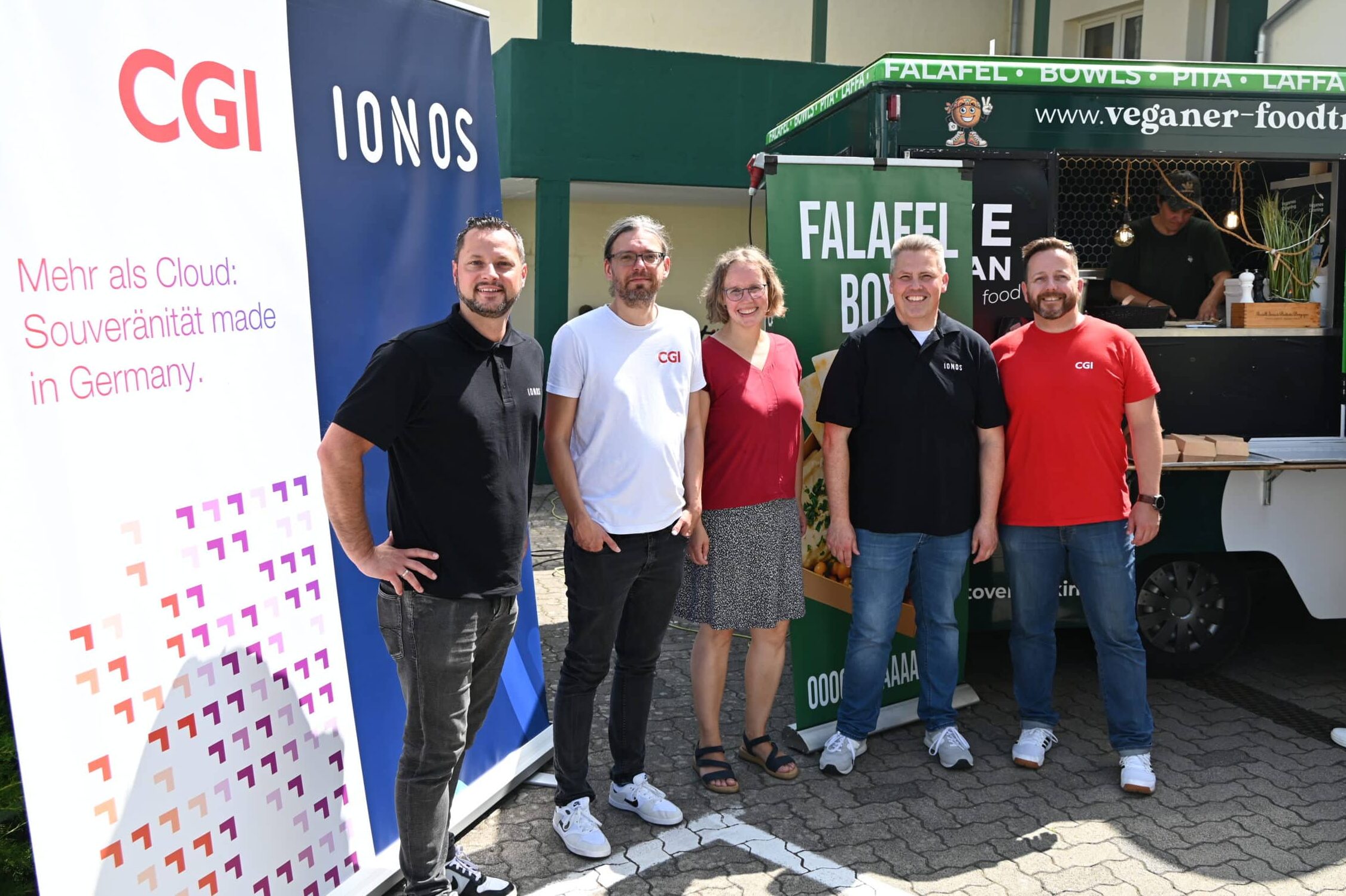 Fünf Personen stehen vor dem Foodtruck und einem großen Aufsteller. Sie lächeln in die Kamera. Von links nach rechts: Tim Kartali von IONOS, Marco de Friend von CGI, Christina Fleischer die stellvertretende Einrichtungsleitung im Martinshaus, Jens Büttner von IONOS und Frank Scherrer von CGI