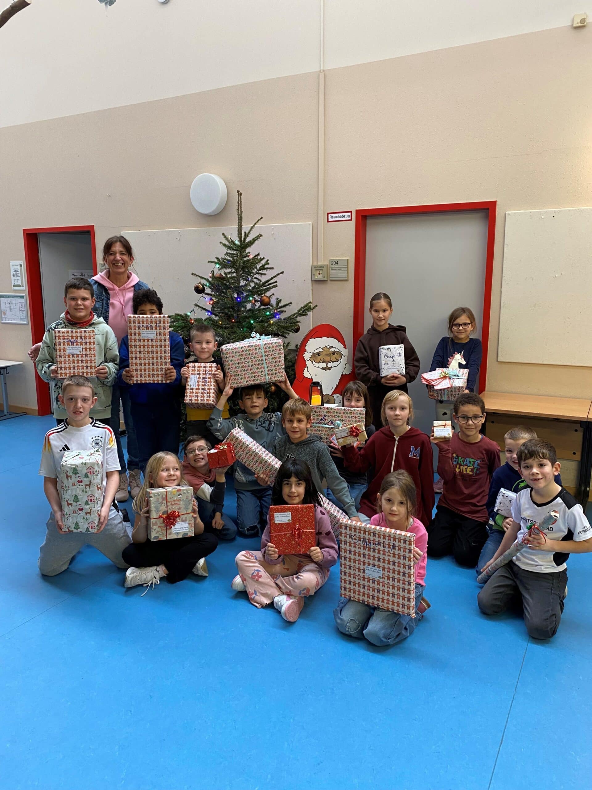 Quelle: BLV 14 Kinder und eine Lehrerin stehen nebeneinander. Sie halten Weihnachtsgeschenke in ihren Händen.