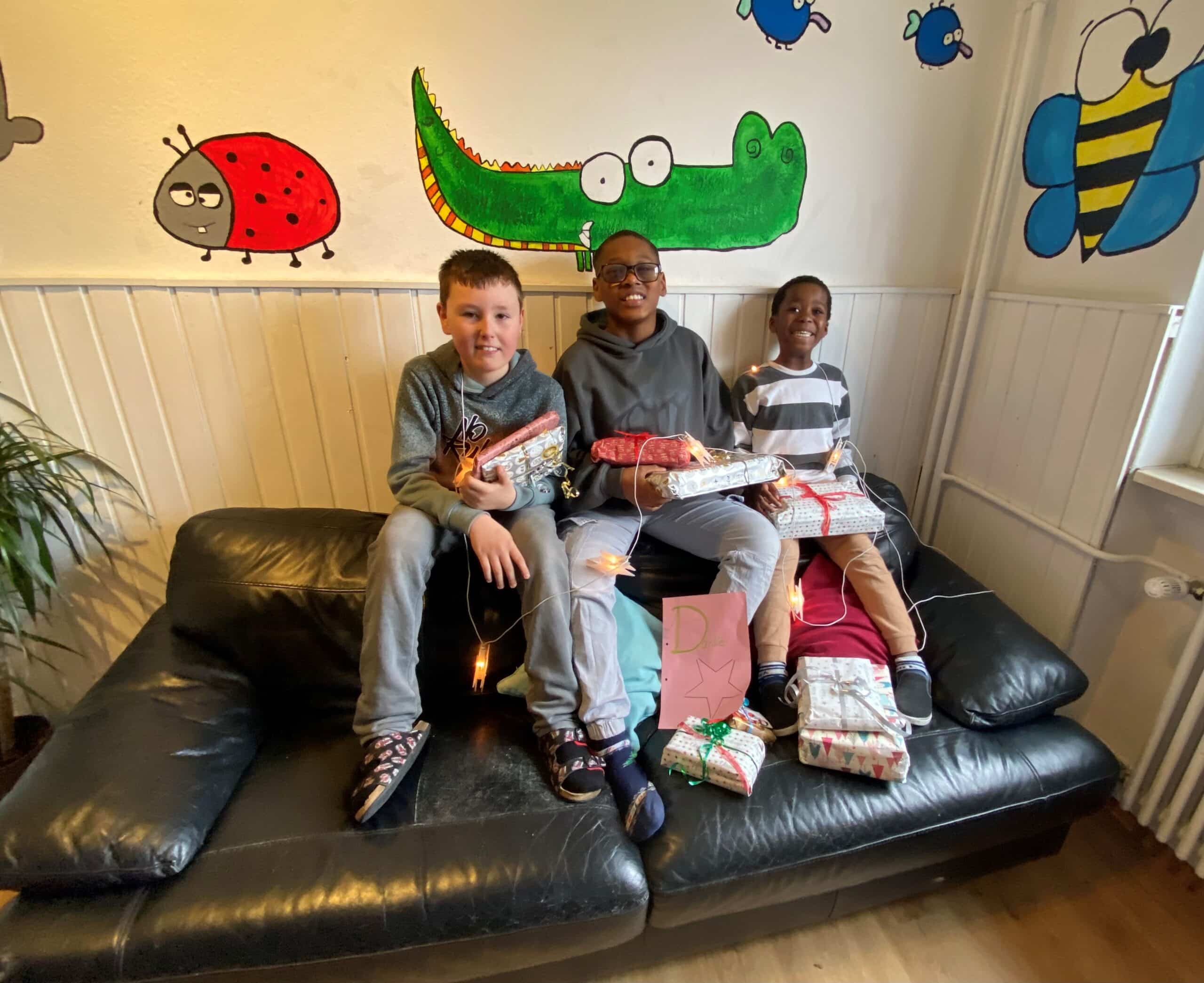 Quelle: BLV Drei Jungen sitzen auf einem Sofa. Sie halten Weihnachtsgeschenke in den Händen und lachen.