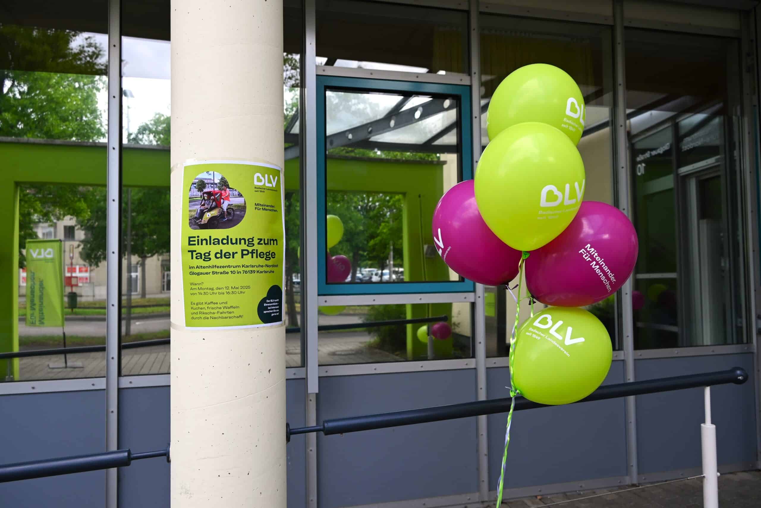 Der Eingang der Pflegeeinrichtung Altenhilfezentrum Karlsruhe-Nordost ist mit grünen und lila Luftballons geschmückt und ein Plakat zum Tag der Pflege ist aufgehängt an einer Säule.