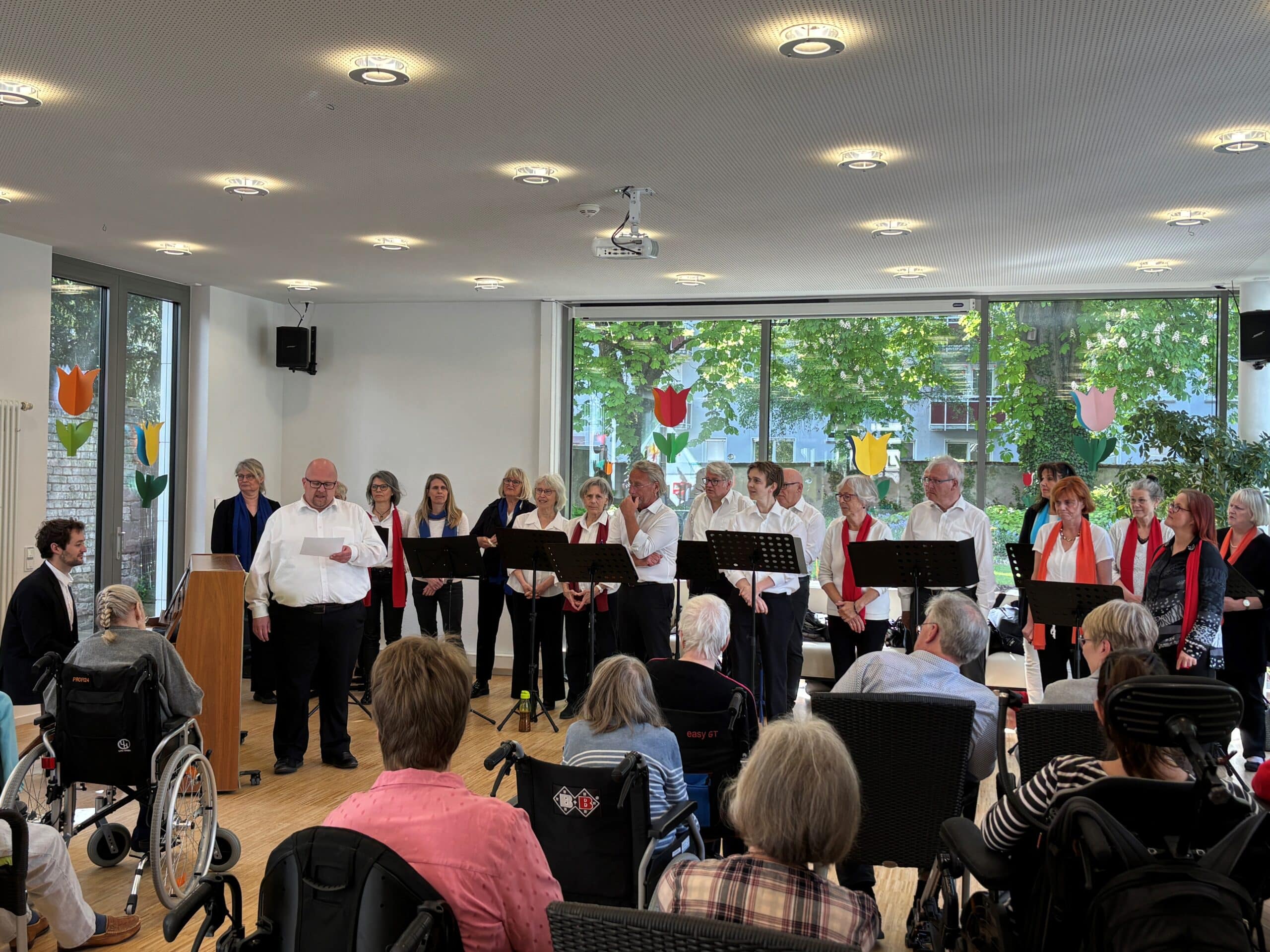 Der Chor bestehend aus über 20 Personen und die Bewohnerinnen und Bewohnern des Friedensheims hören dem Chorleiter zu.
