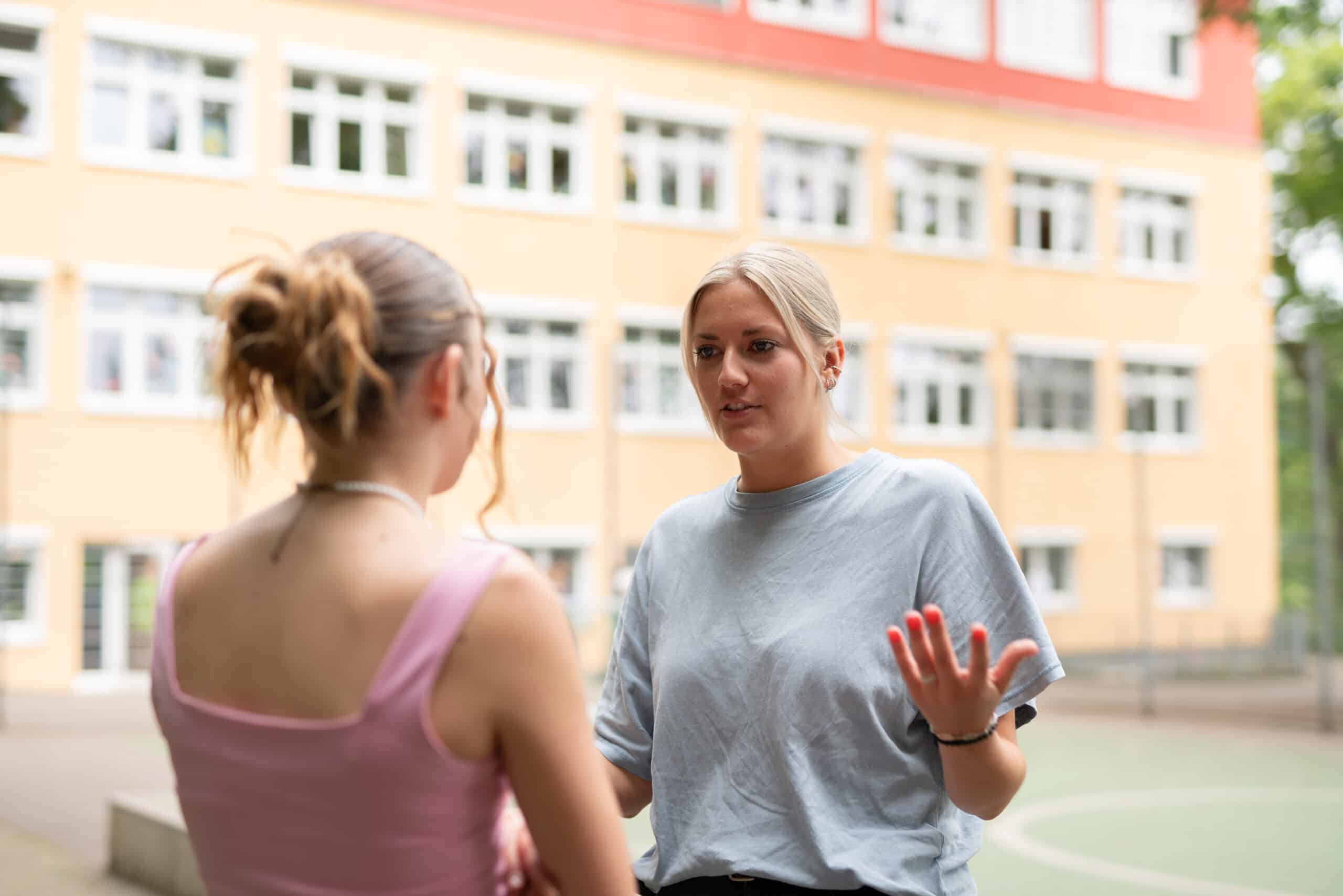 Quelle: BLV eine erwachsene Frau und ein Mädchen sprechen miteinander. Im Hintergrund ist die Schule Enzberg zu sehen.